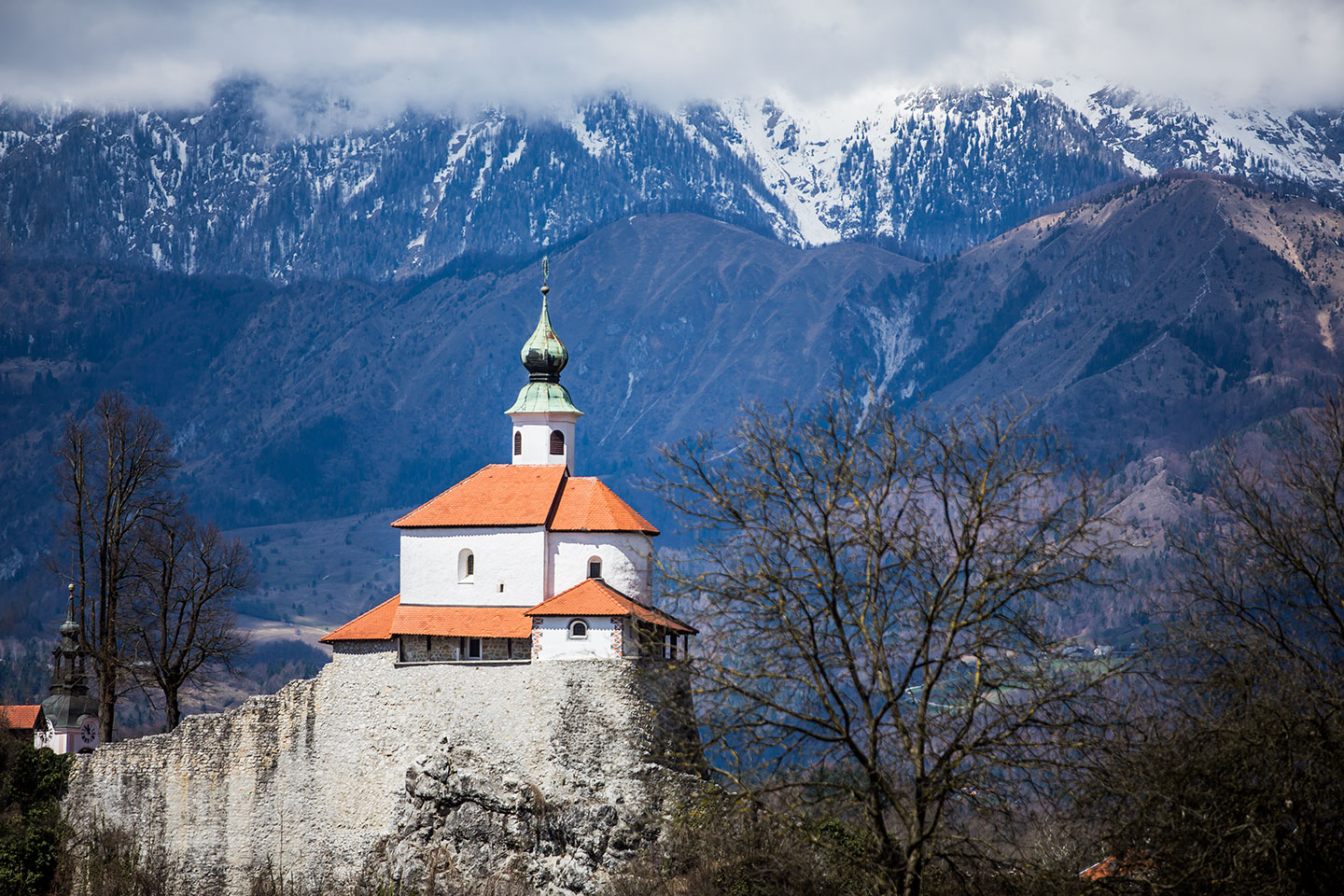 Kamnik, Slovenia Little chapel on a rock with snow capped mountains in the back in Kamnik, Slovenia